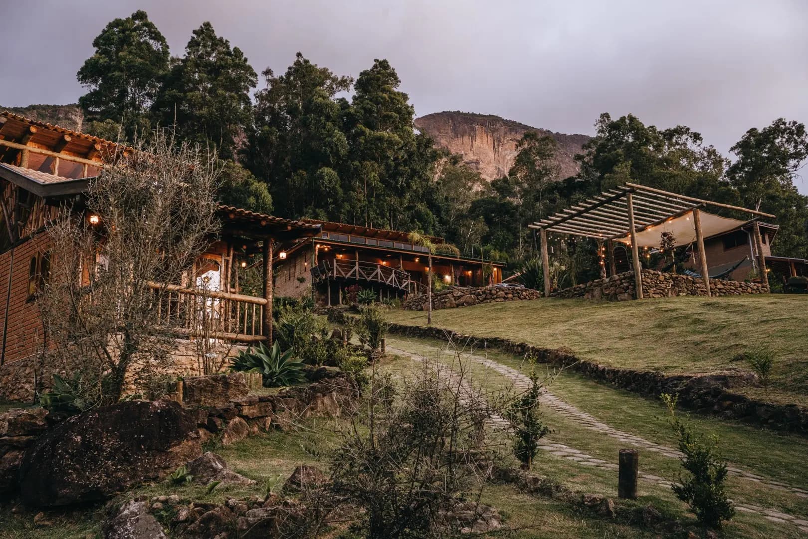 Chalés de madeira e tijolo iluminados ao entardecer, com o paredão da Pedra do Baú ao fundo