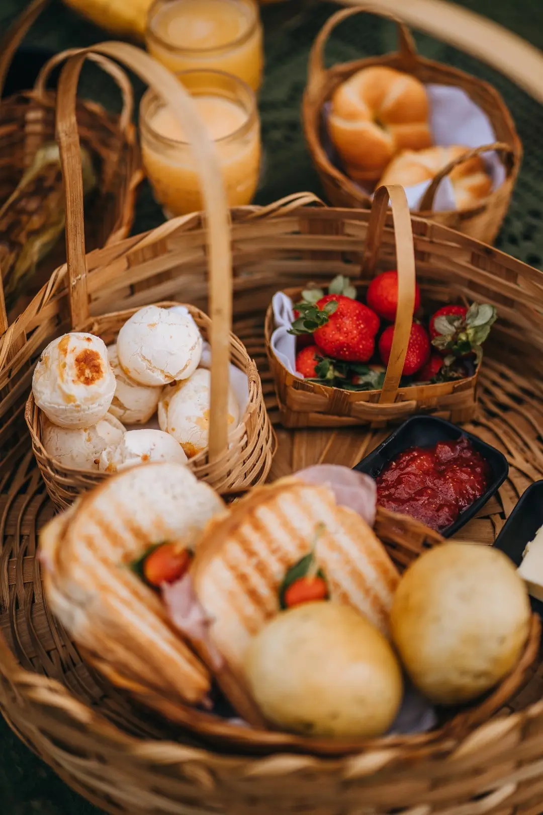 Cesta de café da manhã com pães de queijo, morangos, sanduíches na chapa e sucos